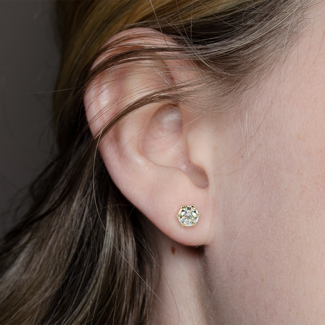 Close-up of a 0.5 carat round moissanite stud earring in a 14k gold-filled setting worn in a model’s ear.