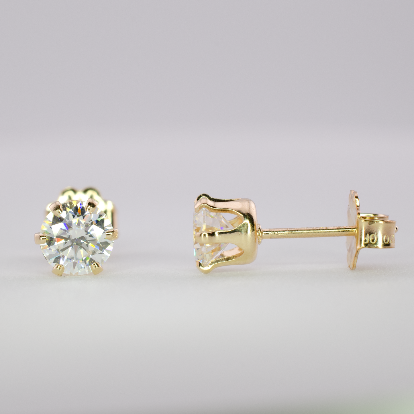 Close-up of two 0.5 carat round brilliant moissanite stud earrings in 14k gold-filled settings, one facing front and one shown sideways.